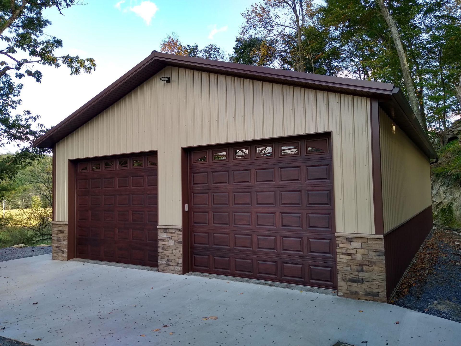 Brown two-car garage with tan siding and stone accents on a concrete driveway