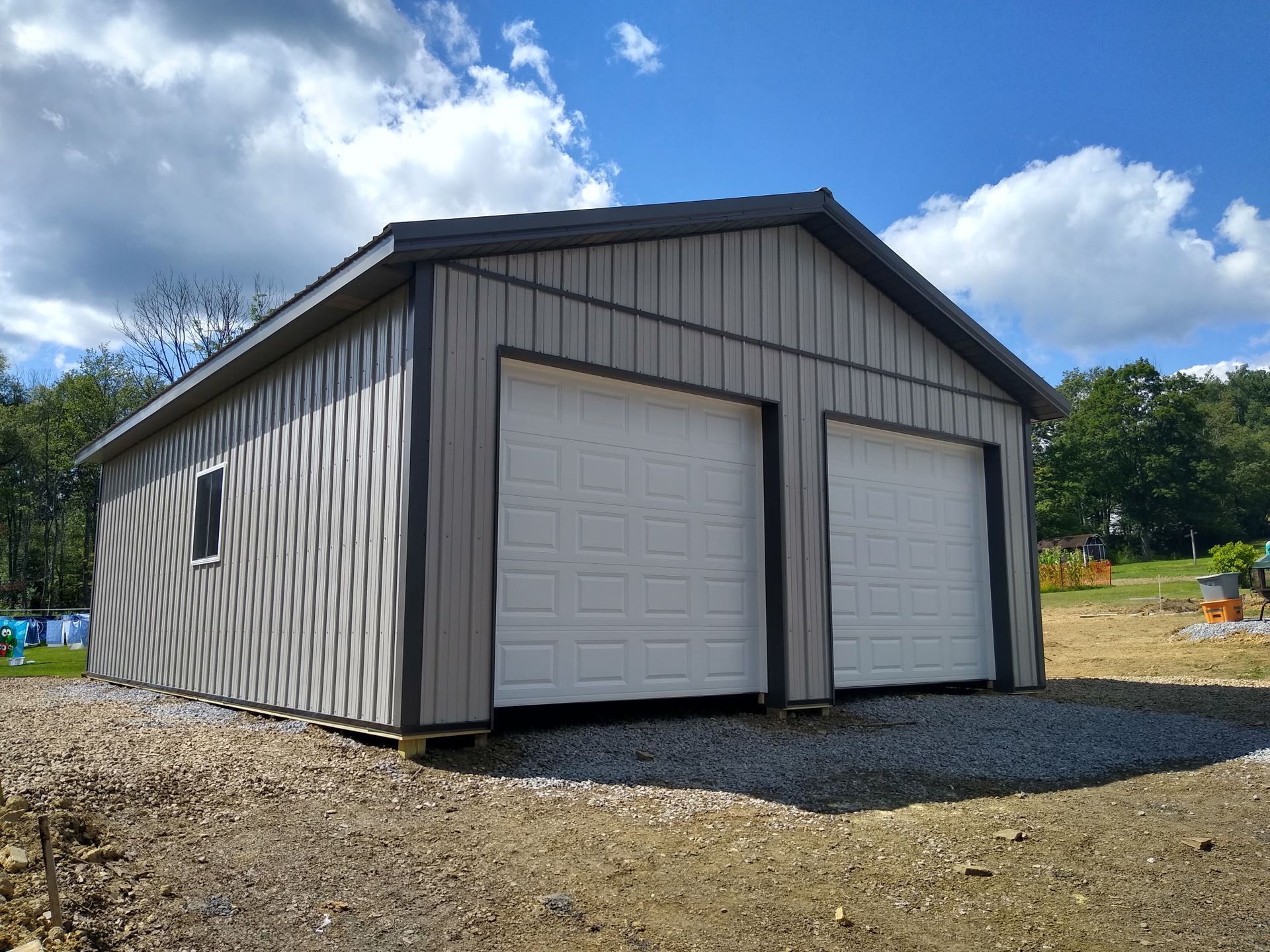 Two-car detached garage with beige siding and white doors on a gravel lot under a blue sky