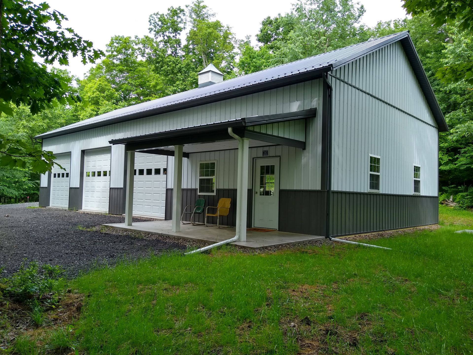 Metal-sided barn-like building with white garage doors and a covered porch in a grassy area