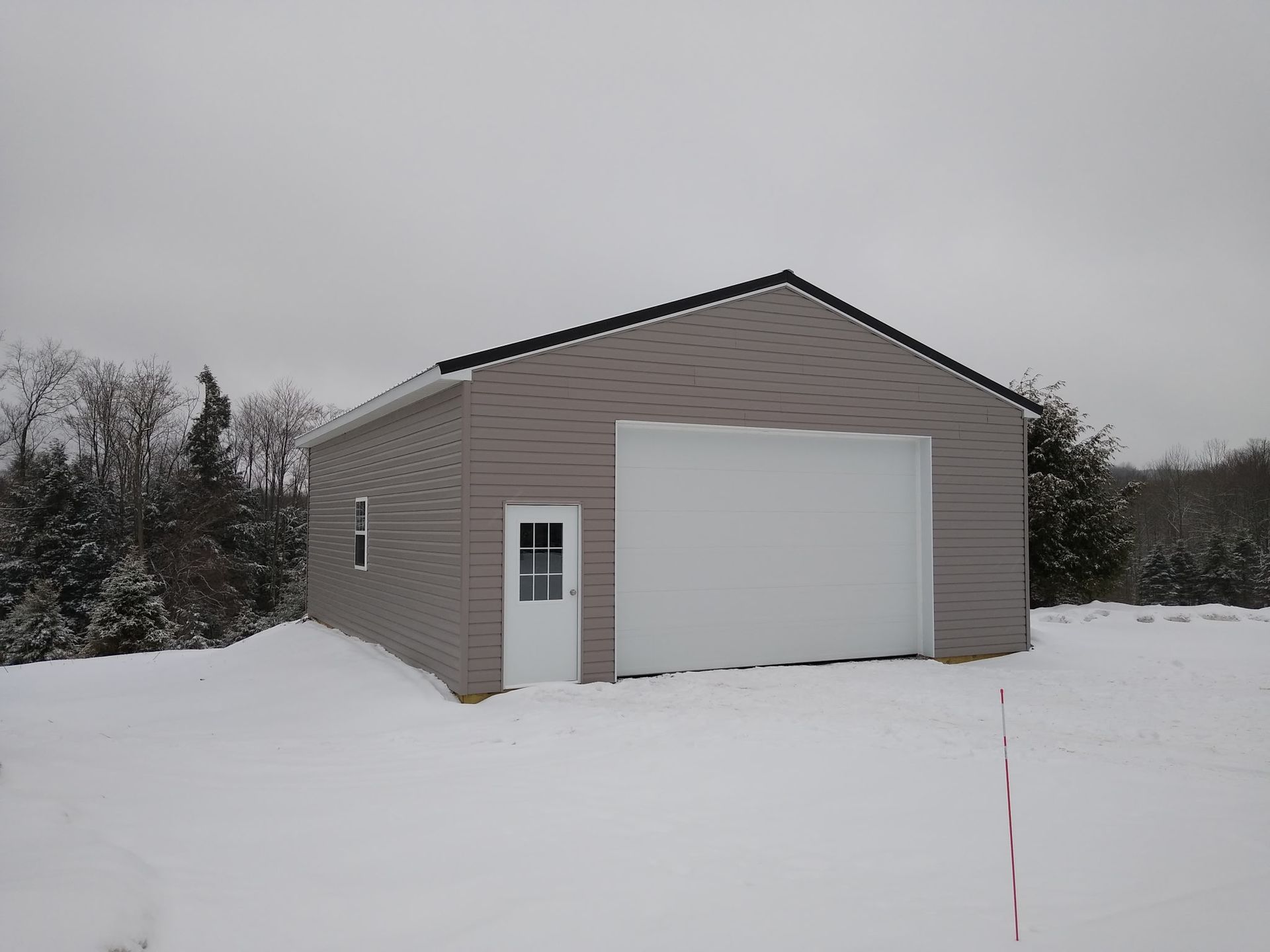 Snow-covered beige garage with a white door and side entry, set against a cloudy winter sky.