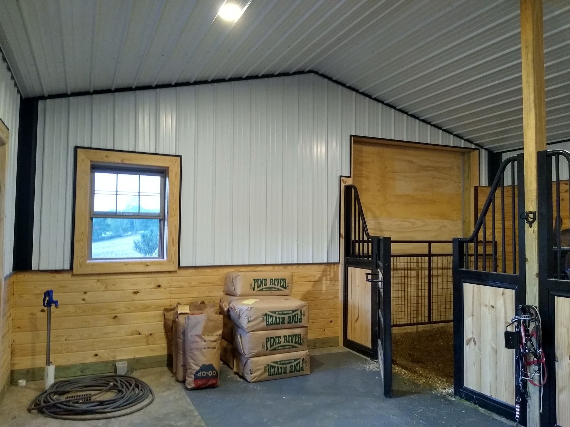 Small indoor stable with wood-paneled walls, a window, and black metal horse stalls.