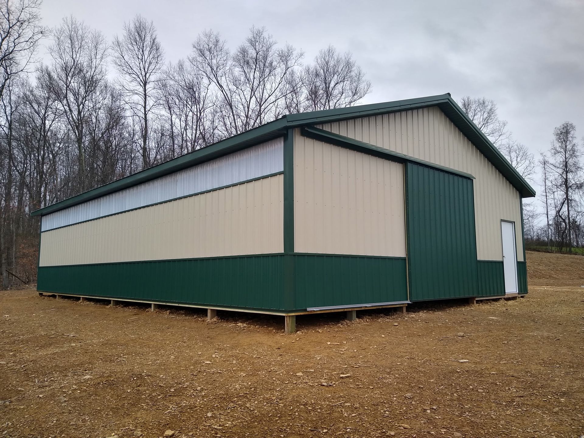 Large beige and green barn-style building on a gravel lot with trees in the background