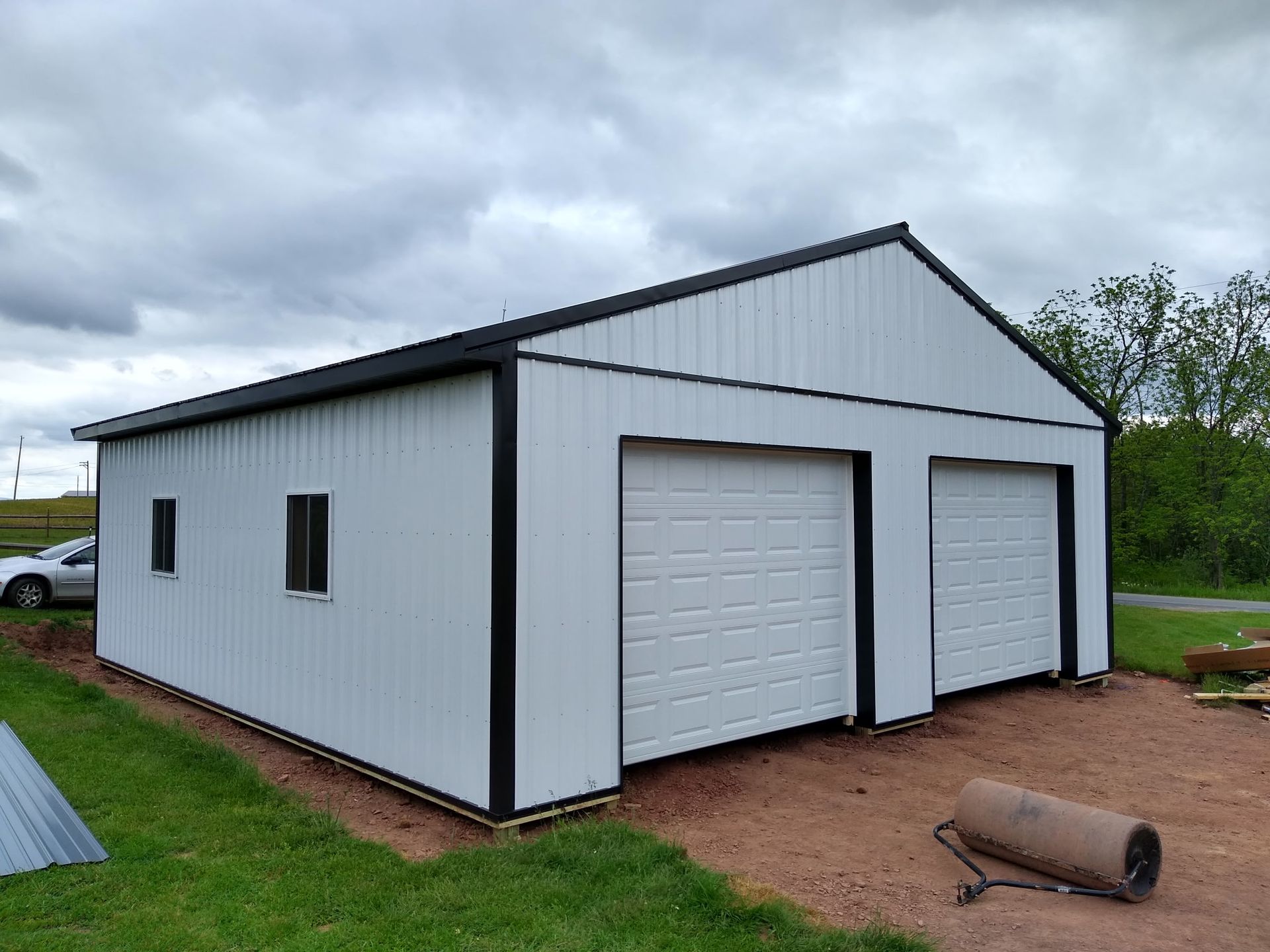 White metal garage building with two roll-up doors on a grassy lot under a cloudy sky