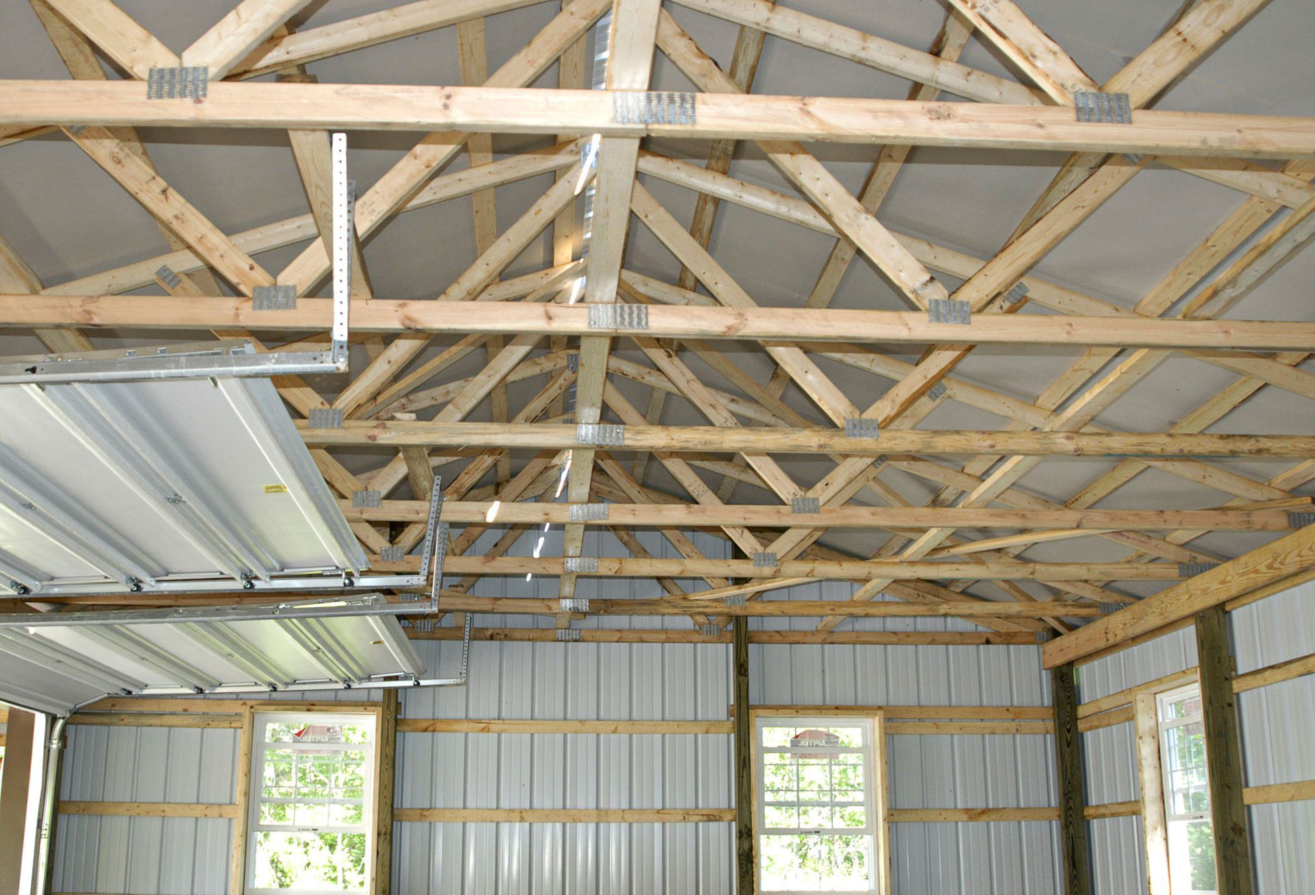 Interior view of a building under construction, showing wooden roof trusses, metal siding, and window frames.