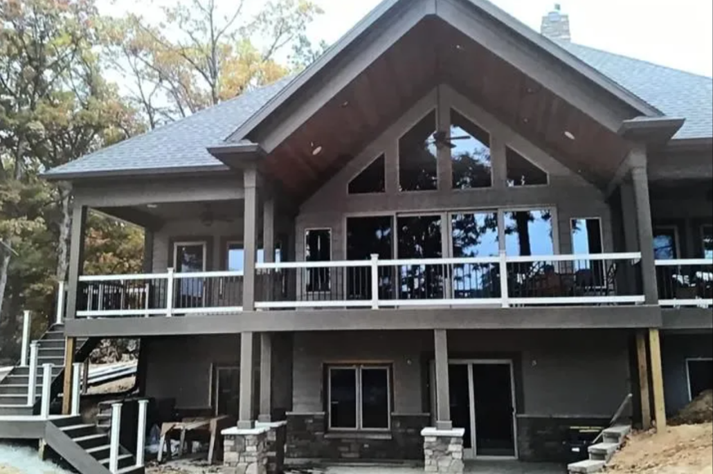 Two-story house with tan siding, white trim, and a person on the roof.