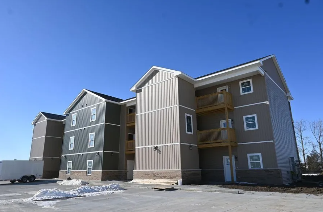 Blue house with white trim, red accents, and gray shutters against a bright blue sky.