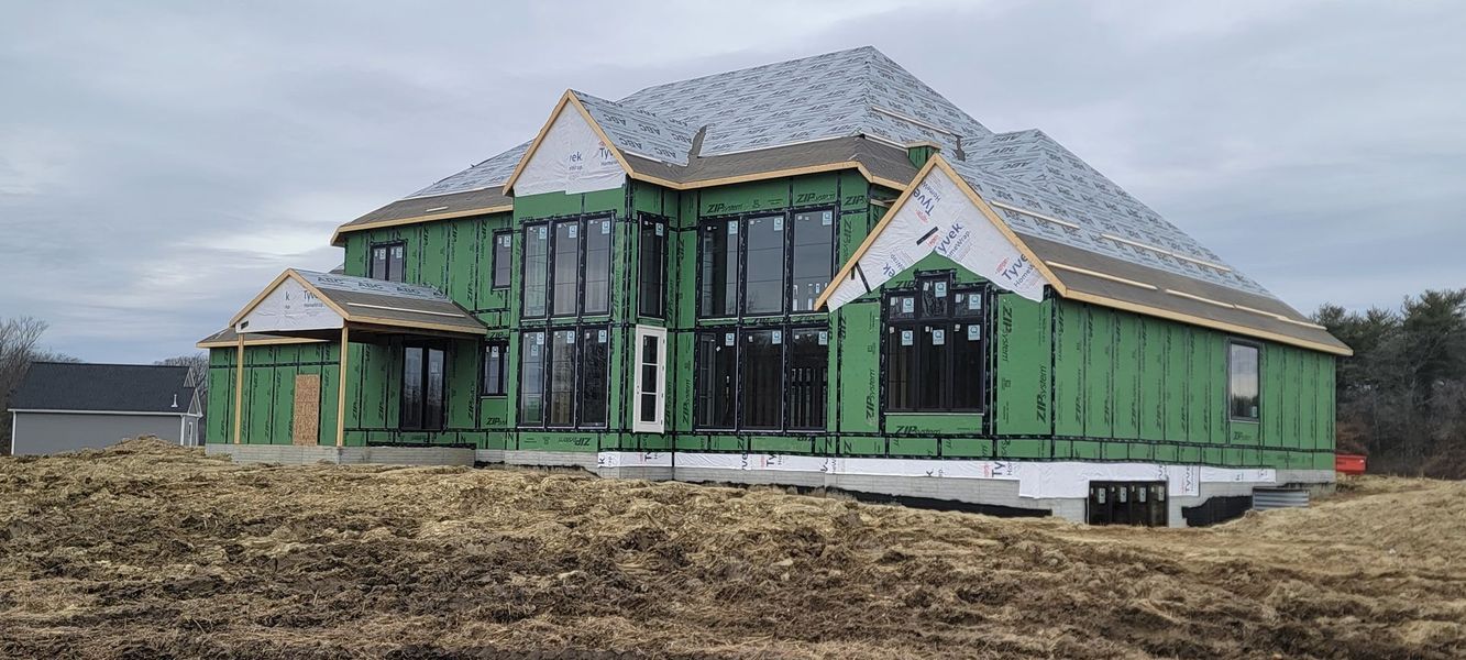 House under construction with green siding and large windows on a cloudy day.