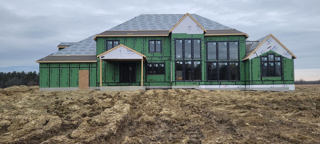 House under construction with green siding and grey roof. Brown dirt in foreground. Overcast sky.