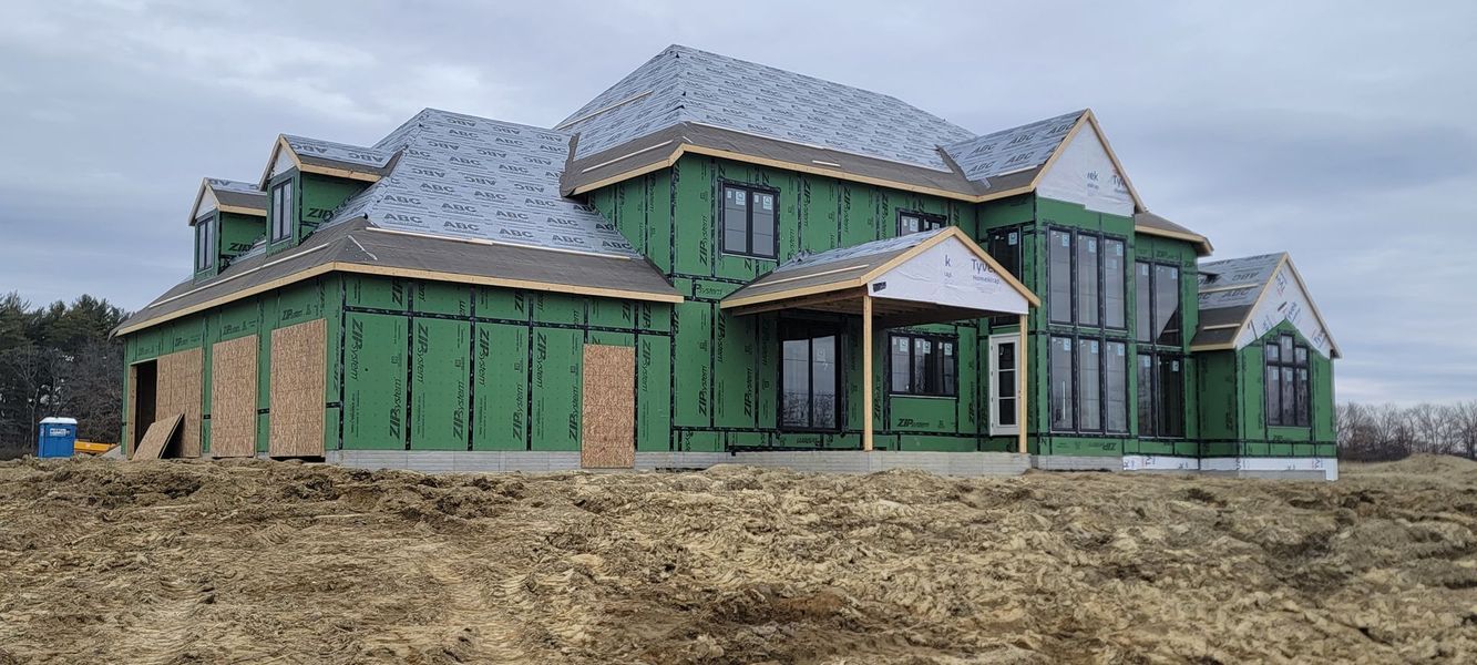 House under construction; green siding, grey roof, cloudy sky.