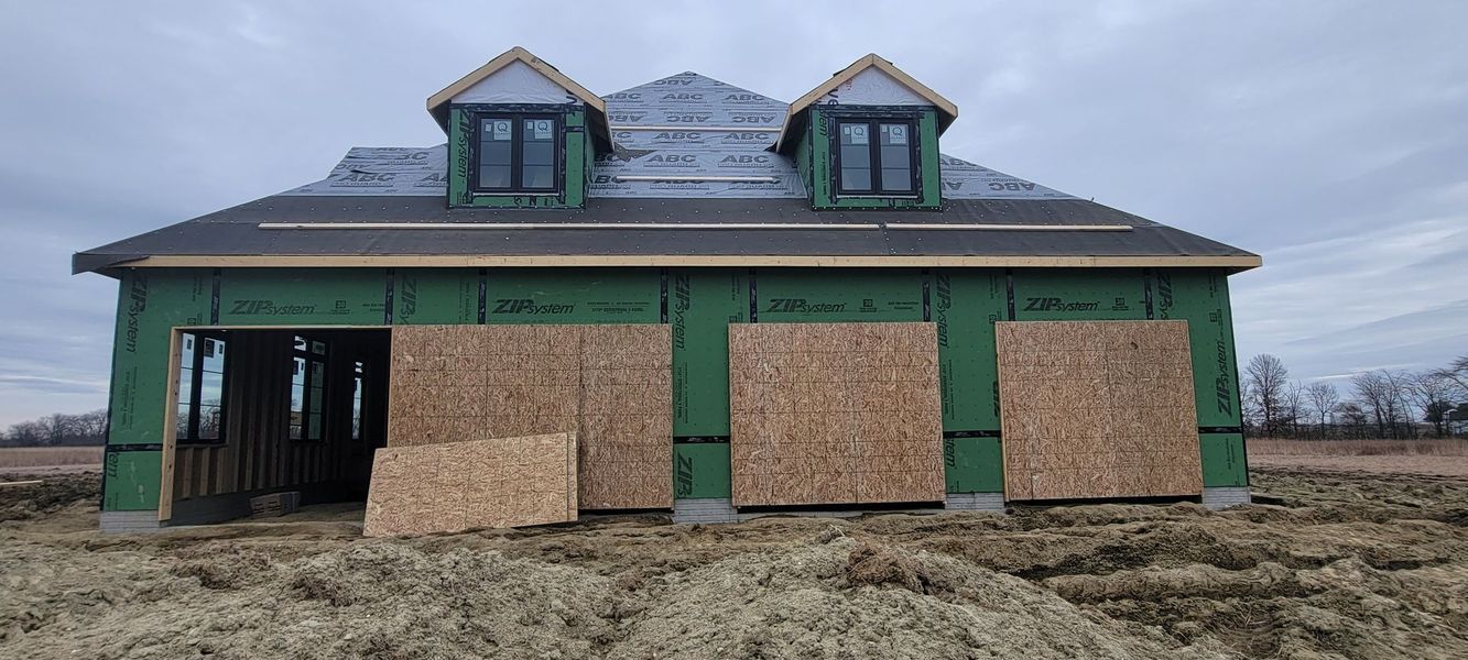 A house under construction, with OSB boards covering window openings, green siding, and two dormers.