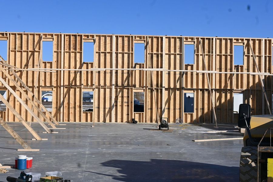 Wood frame building under construction, with window openings. Construction equipment and clear sky.