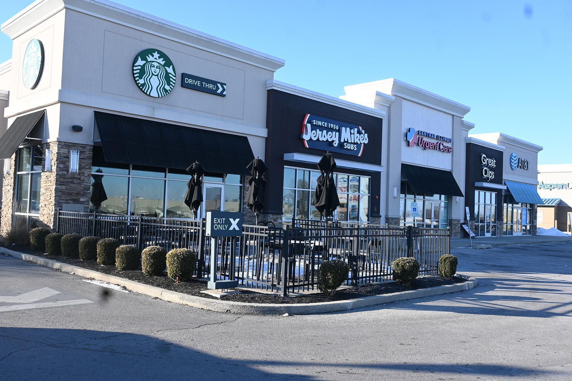 Exterior of a strip mall with a Starbucks, Jerry's Subs & Pizza, and another business under a bright blue sky.