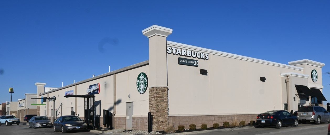 Exterior view of a Starbucks building with a drive-thru. Cars parked in front on a clear, sunny day.