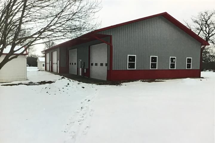 Snowy scene with a large metal building. It has red trim and several garage doors. Windows line one side.