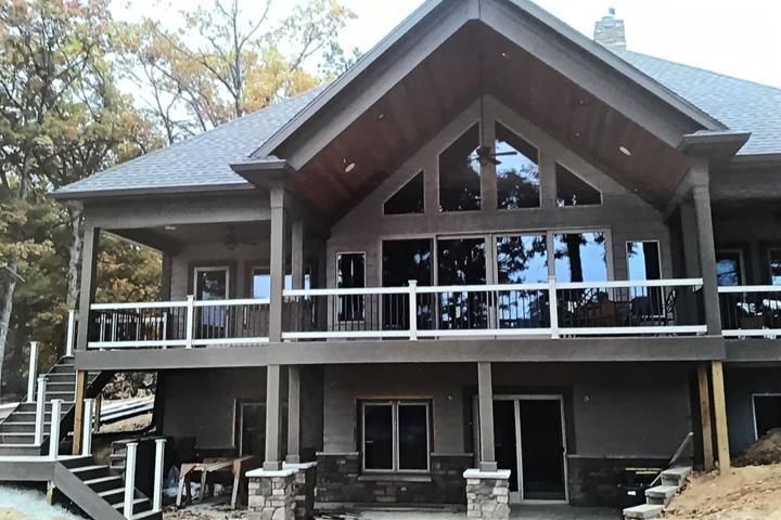 Gray house with a large deck and windows, stone accents, and a sloped roof.