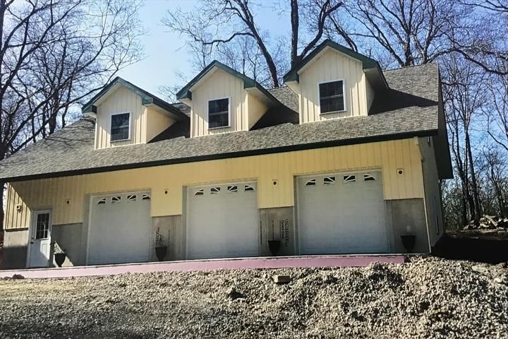 Three-car garage with yellow siding, three dormers, and white garage doors under a gray roof.