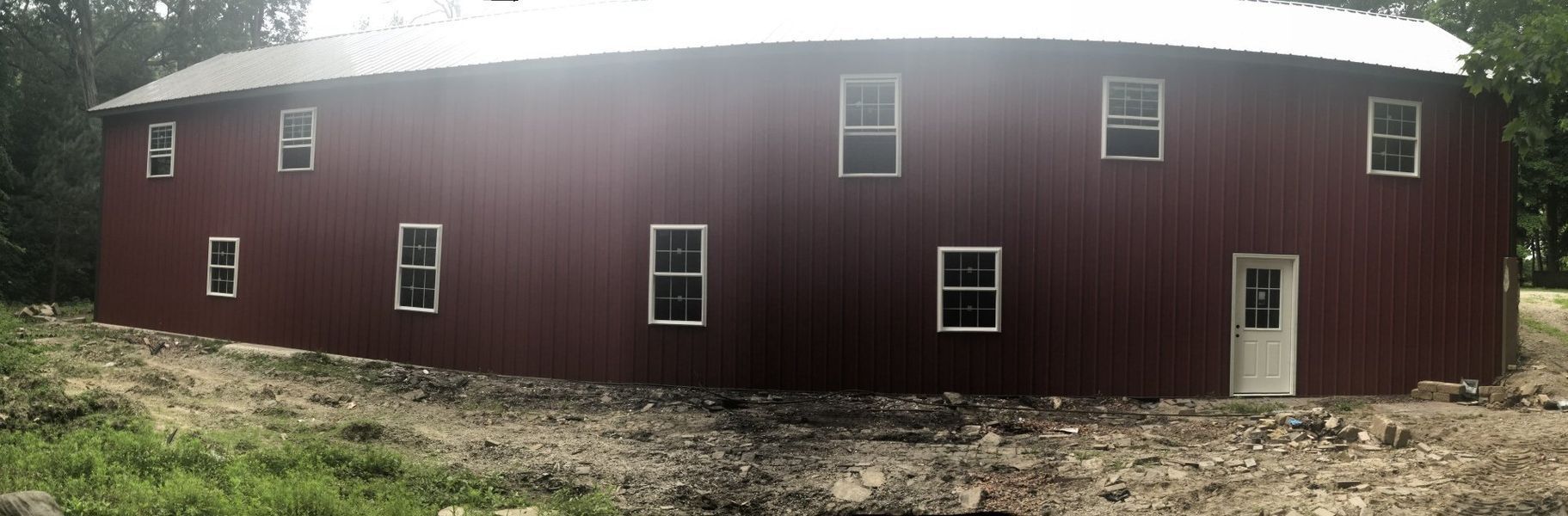 A large, red barn with white-trimmed windows and a white door, set in a yard.