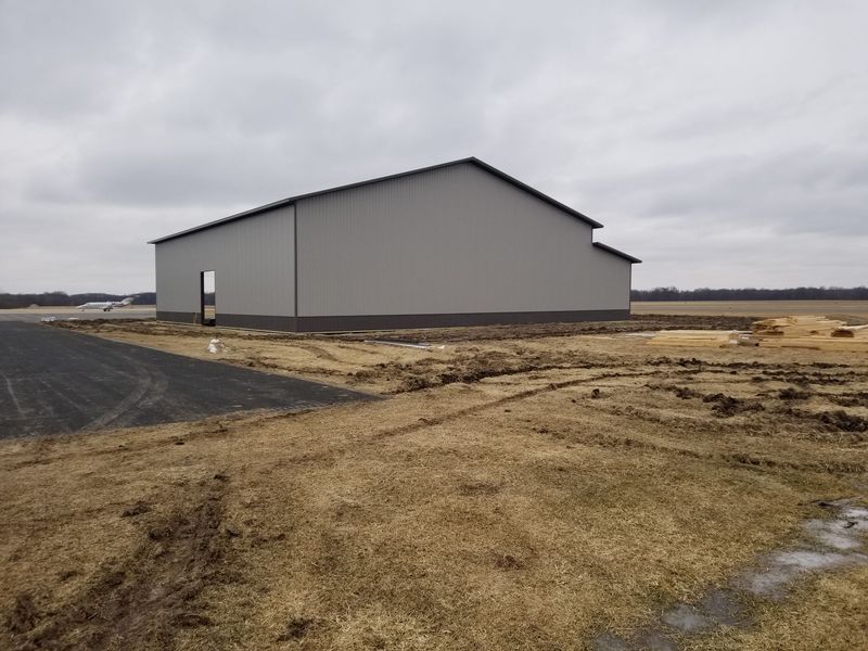Gray metal building with dark trim on a field of brown grass, overcast sky.