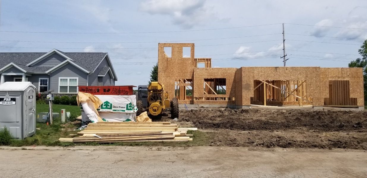 Construction site with a partially built house, next to a finished house, under a cloudy sky.