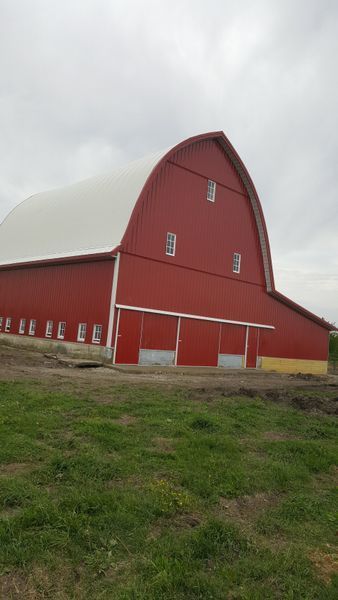 Red and white arched-roof barn on a grassy hill under a cloudy sky.