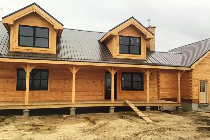 Wooden cabin under construction with porch and dormers, metal roof.