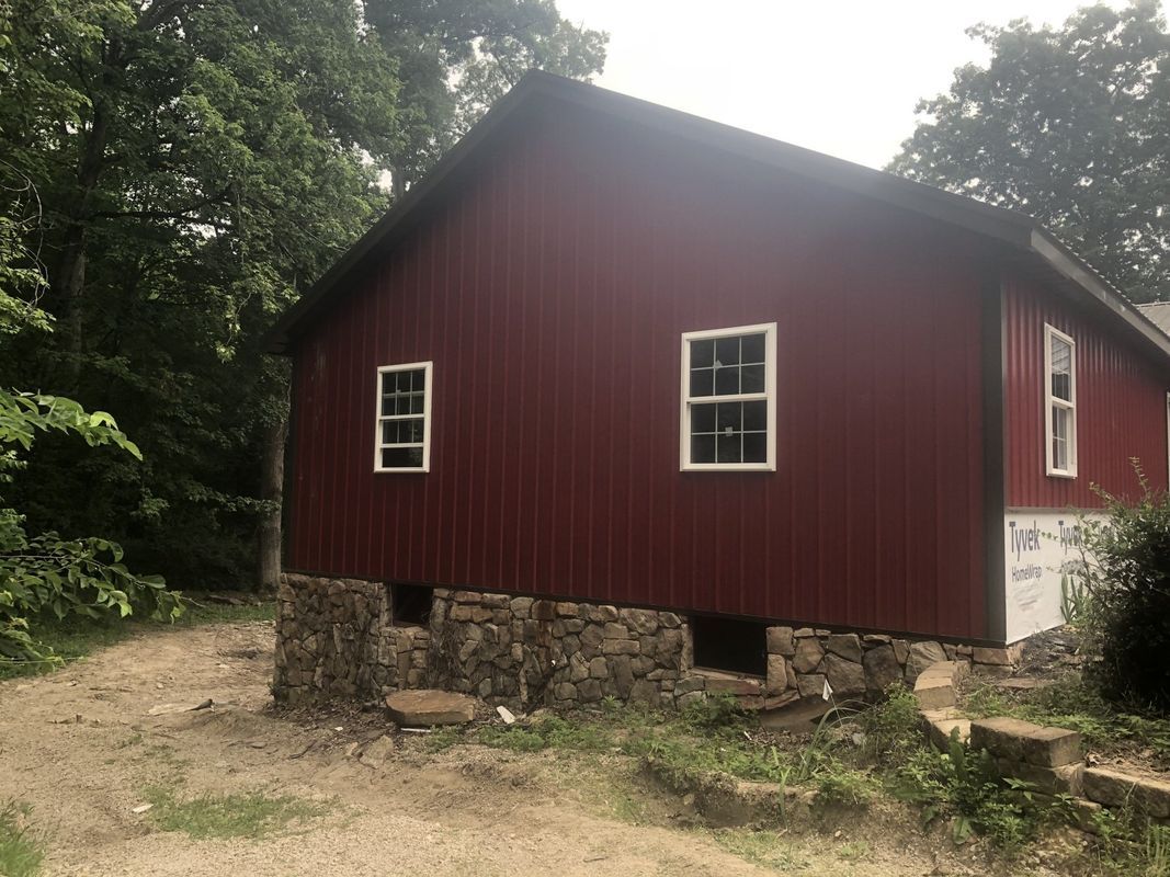 Red building with white-framed windows on a stone foundation, set amongst trees.