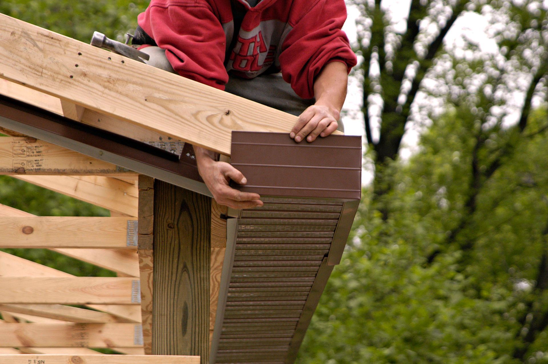 Person installing brown siding on the edge of a wooden structure.