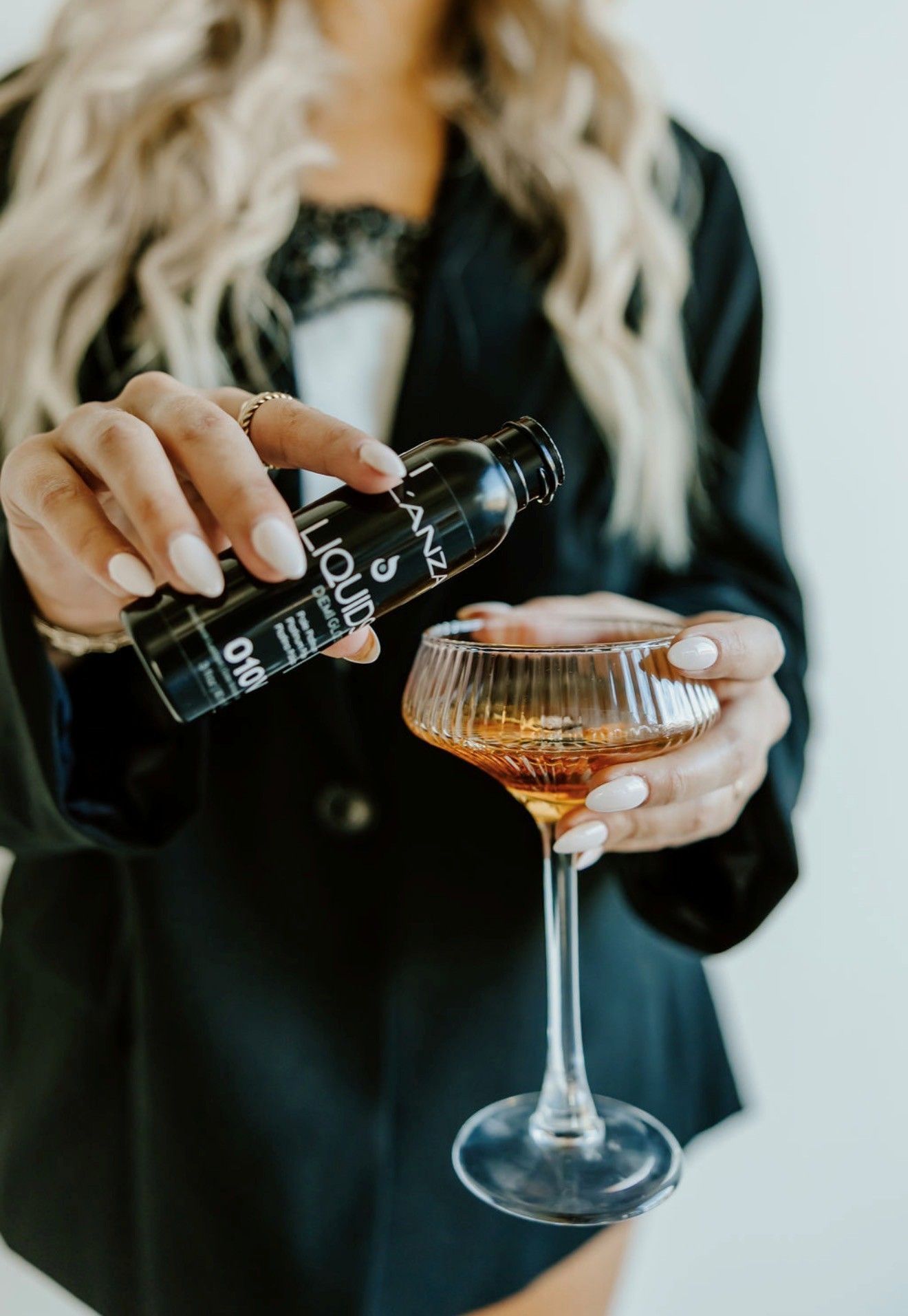Person pouring sparkling wine into a champagne coupe with a black bottle and long blonde hair visible