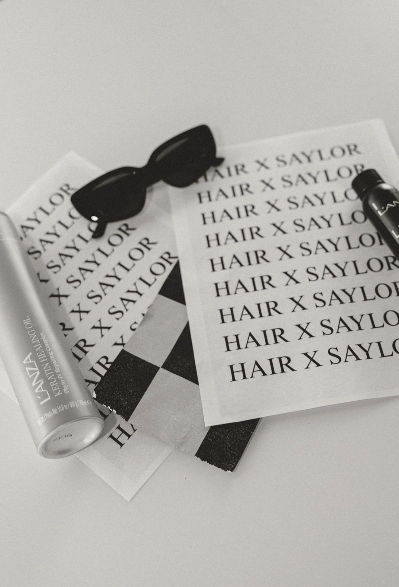 Hair X Saylor beauty products on a light surface, including a tube, bow, and branded cards