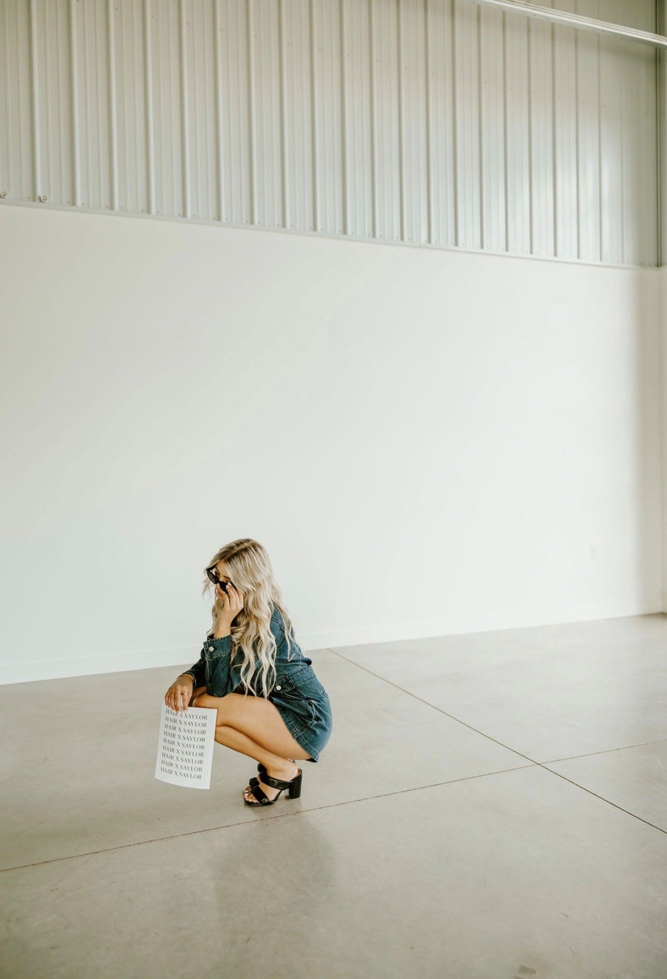 Woman crouching in a bright, empty room holding a patterned bag