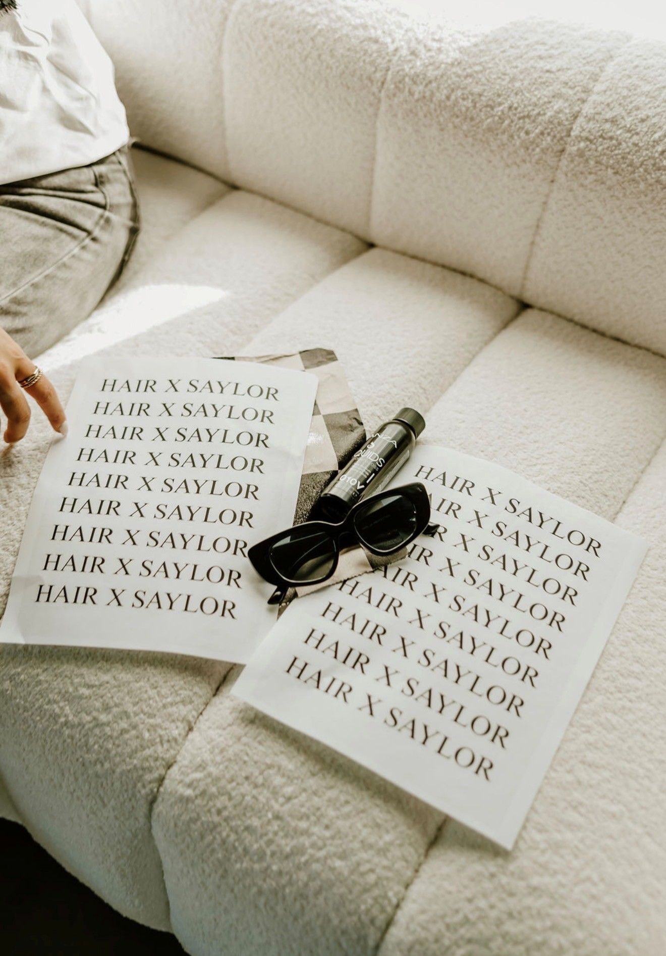 Two sheets on a white couch with black sunglasses, printed with “HARRY STYLES” repeated across them.