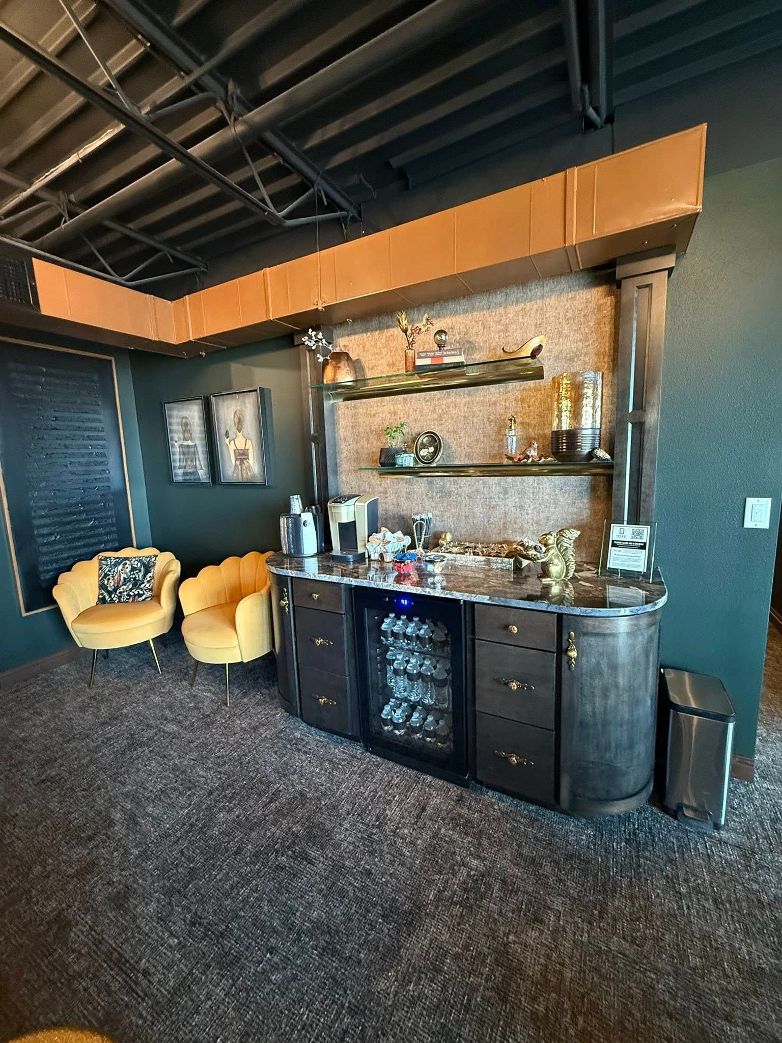 Modern lounge area with yellow chairs, a dark bar cabinet, stone accent wall, and exposed ceiling beams.