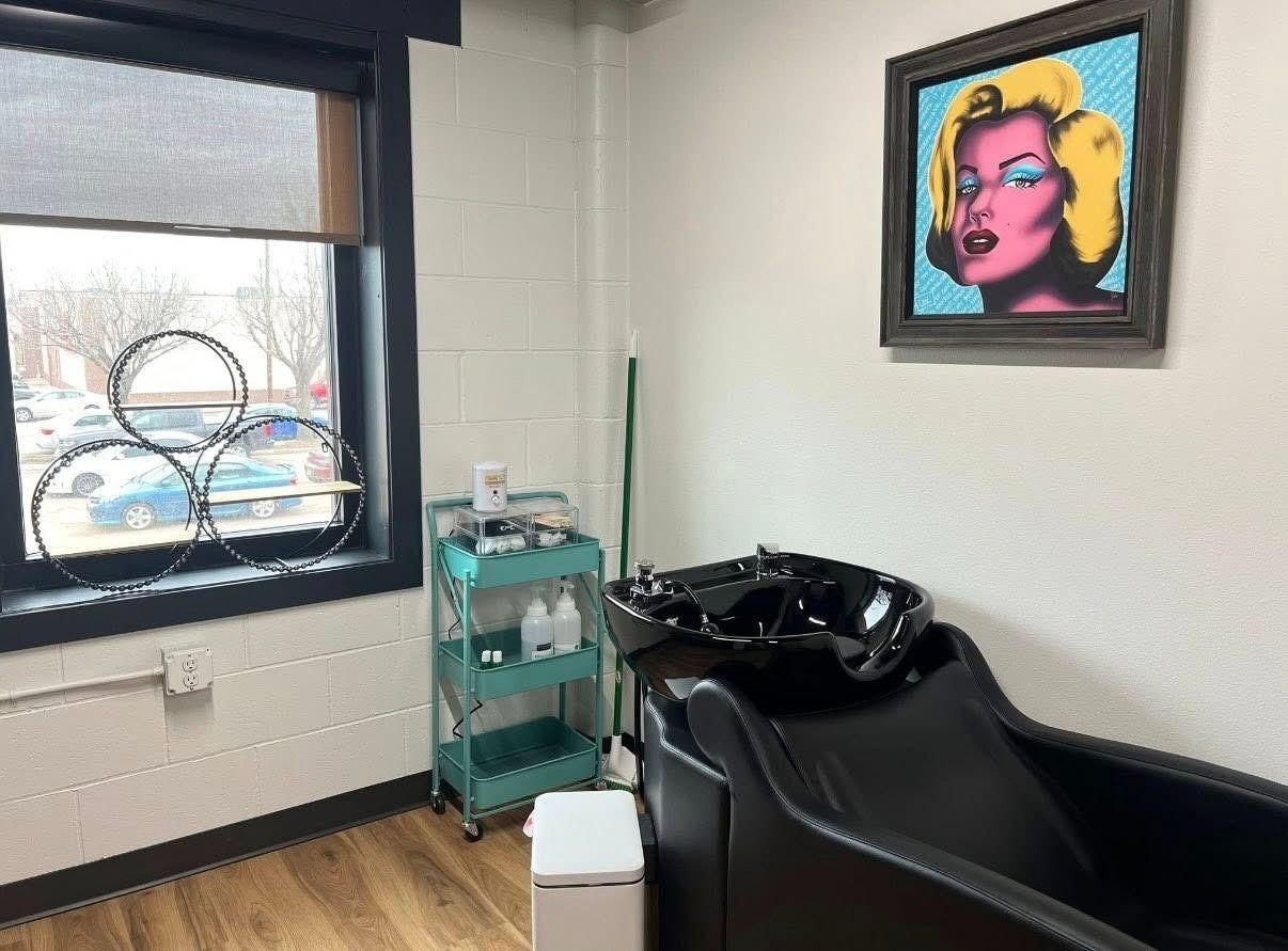 Modern salon with wash basin, teal cart, window, and colorful wall art.