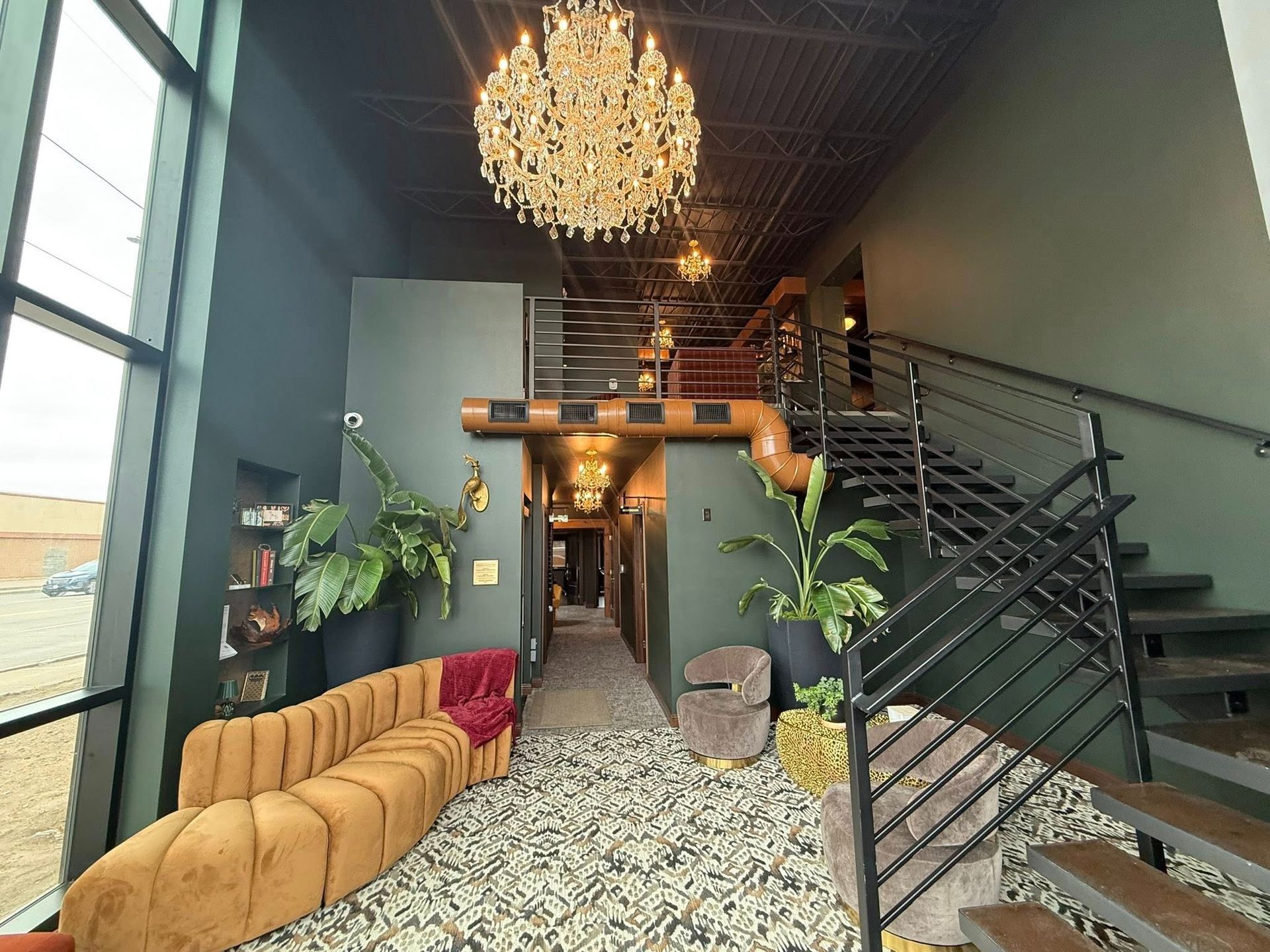 Modern lobby with chandelier, staircase, patterned floor, and mustard sofa under a lofted ceiling.