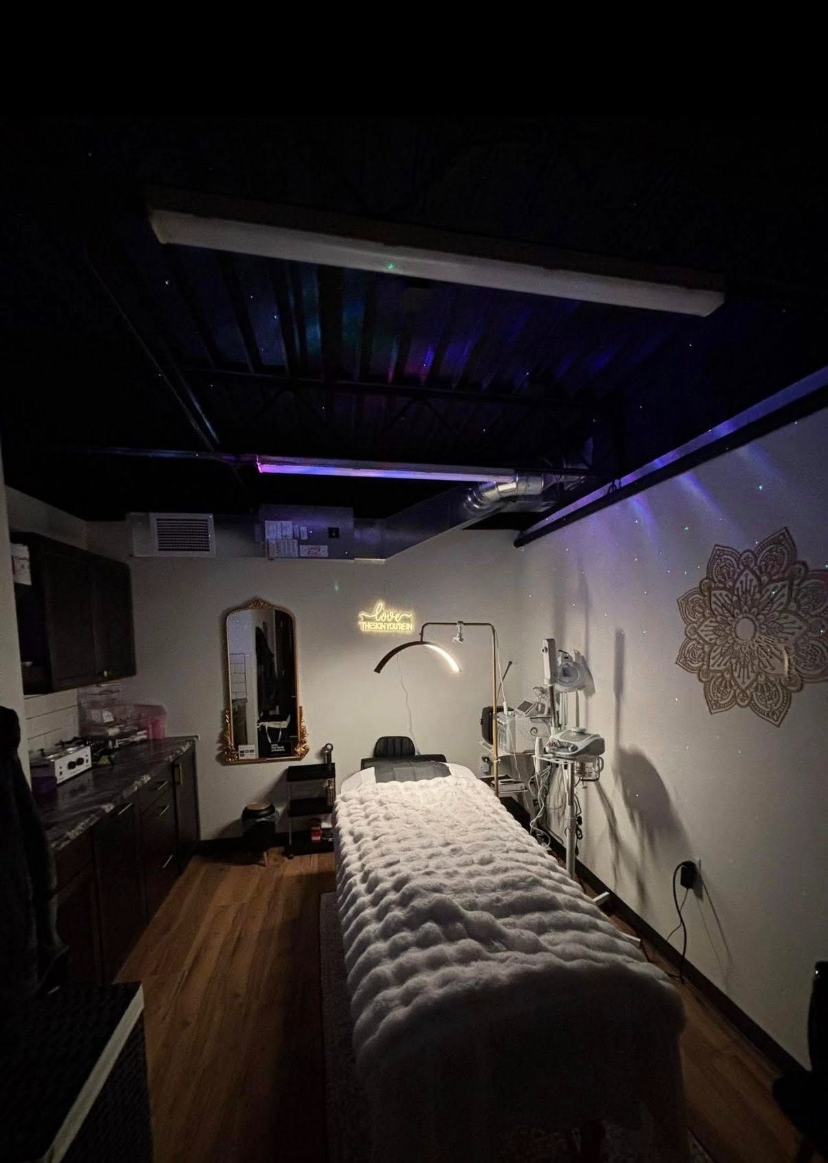 Dim interior with a long padded treatment table, black ceiling lights, and equipment along the walls.
