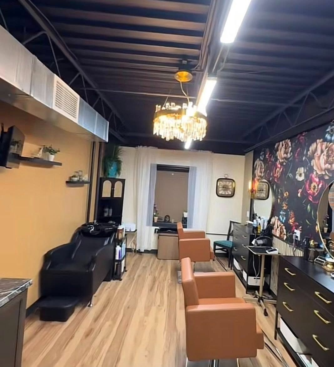 Modern salon interior with black shampoo chair, orange styling chairs, chandelier, and floral wall mural