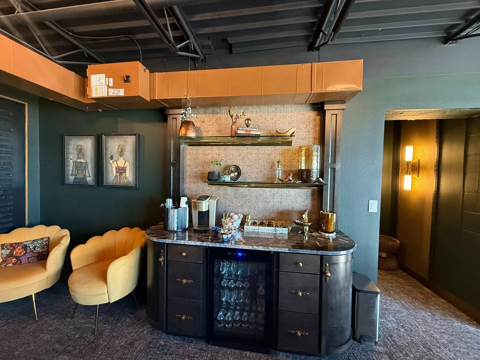 Stylish lounge with bar cabinet, shelves, warm lighting, and cozy seating in a dark teal room