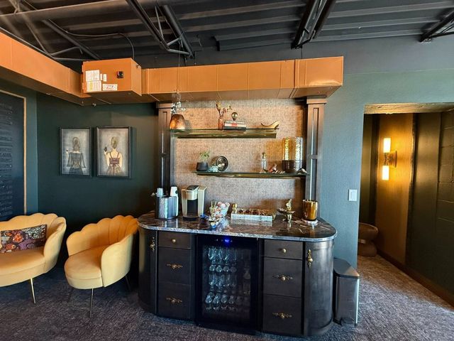 Stylish lounge with dark walls, orange chairs, bar cabinet, shelves, and warm hallway lighting
