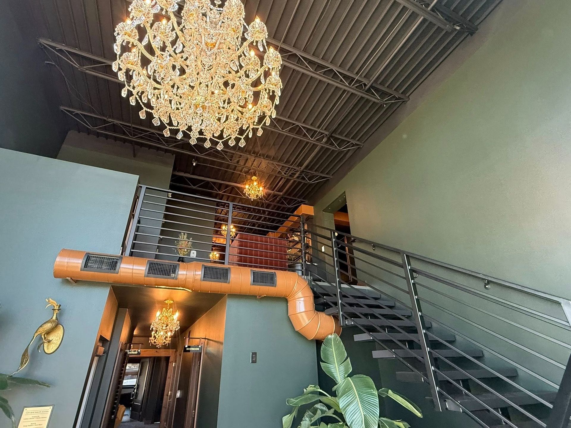 Modern interior with grand staircase, chandelier, and exposed ductwork under a high ceiling
