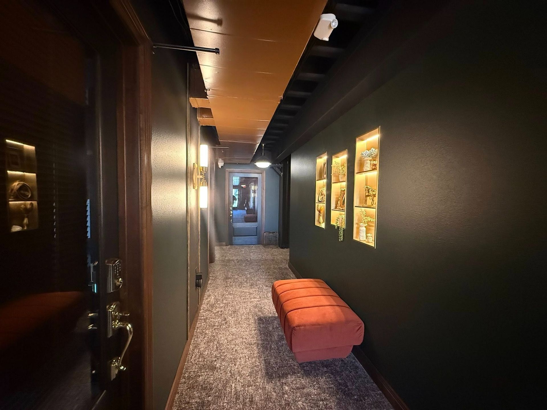 Narrow dim hallway with framed wall art and an orange bench at the end