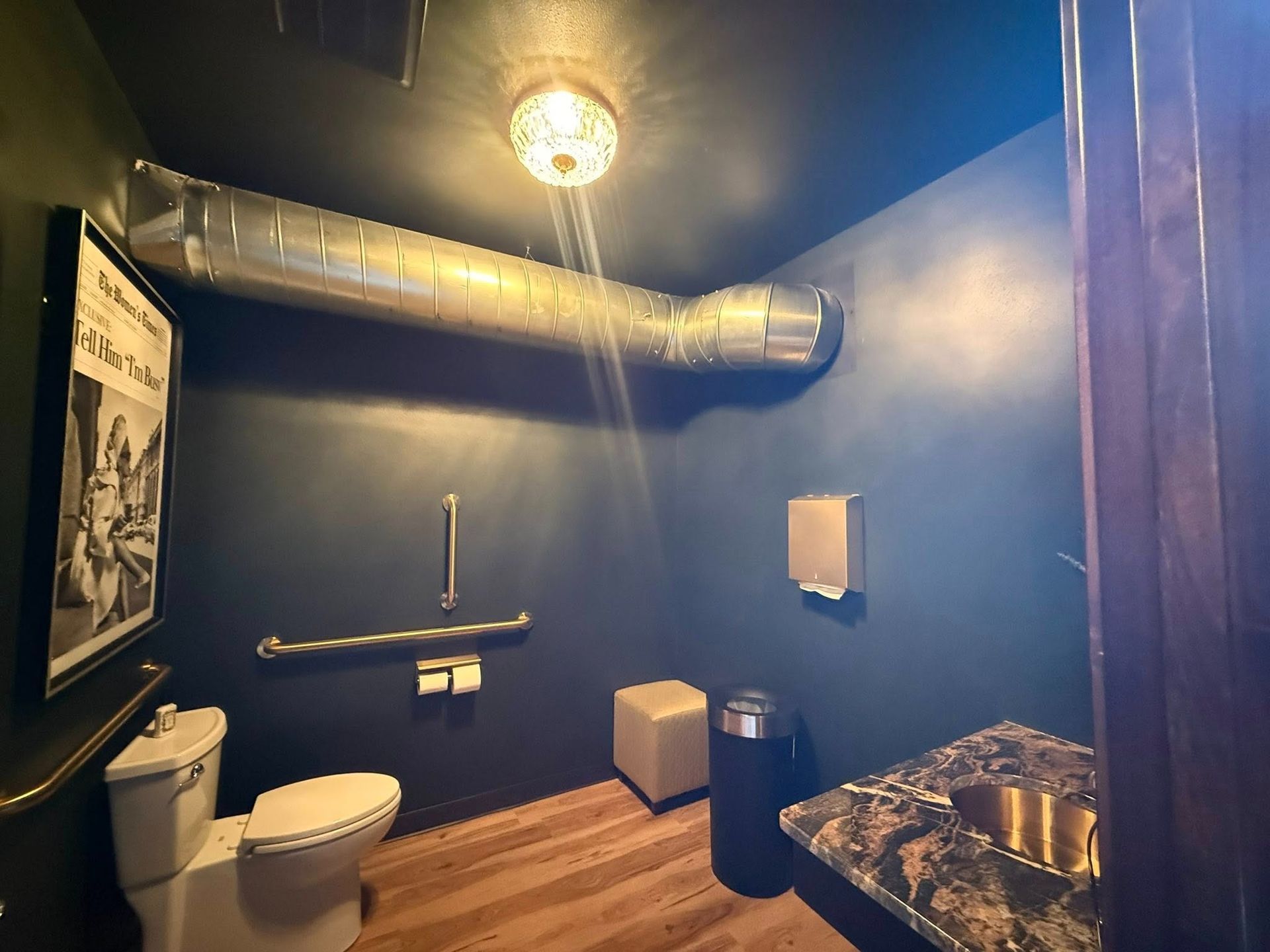 Small industrial-style restroom with toilet, sink, blue walls, exposed ductwork, and checkered floor.