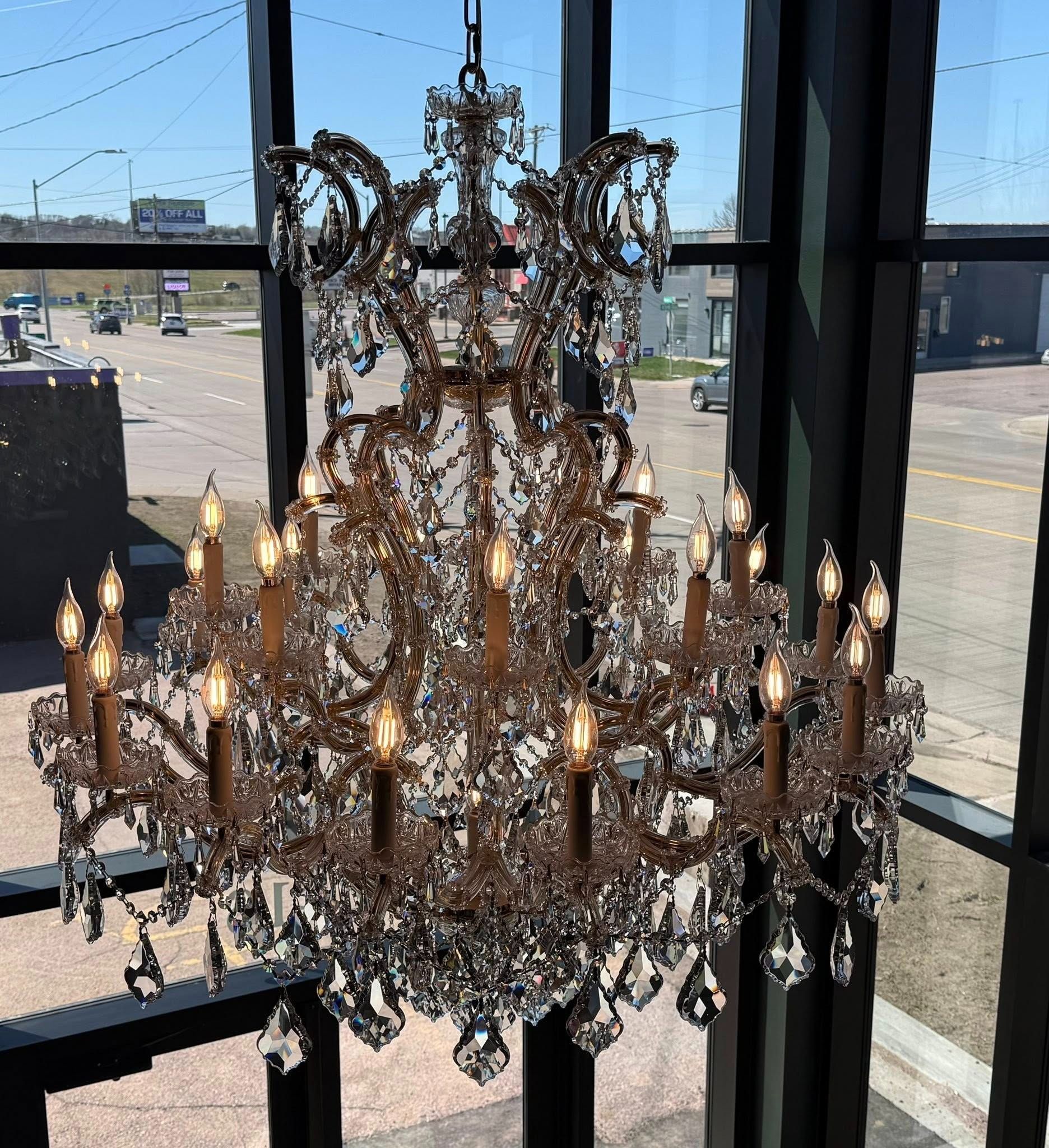 Ornate crystal chandelier hanging in front of a large window with daylight outside