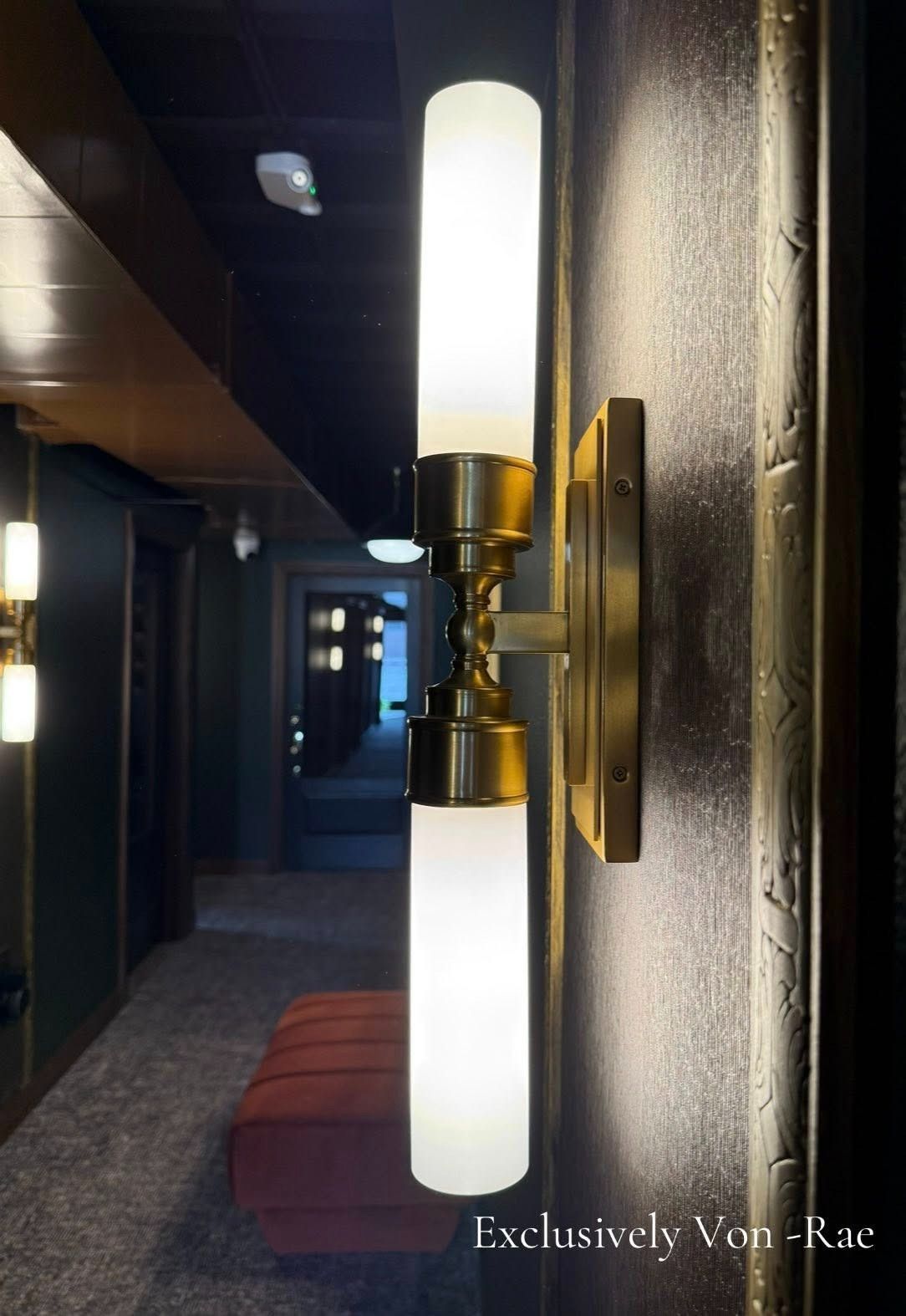 Dim hallway with a brass wall sconce casting warm light against a textured gray wall.