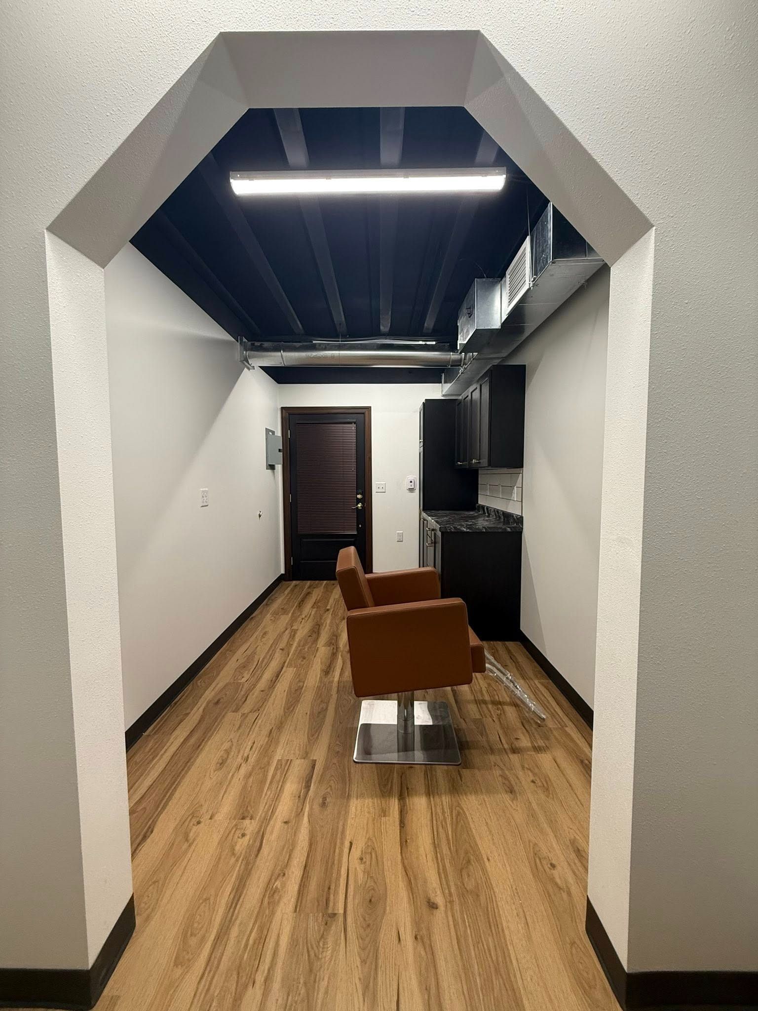 Long hallway with wood flooring, arched opening, and a brown chair in the center.