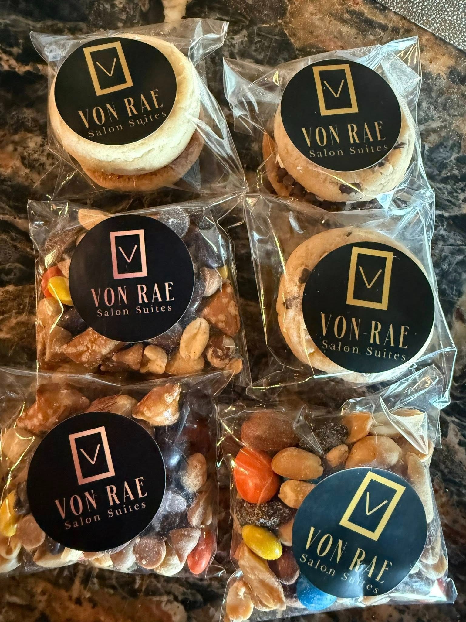 Six packaged assorted snacks with black and gold “VON RAE” labels on a display.
