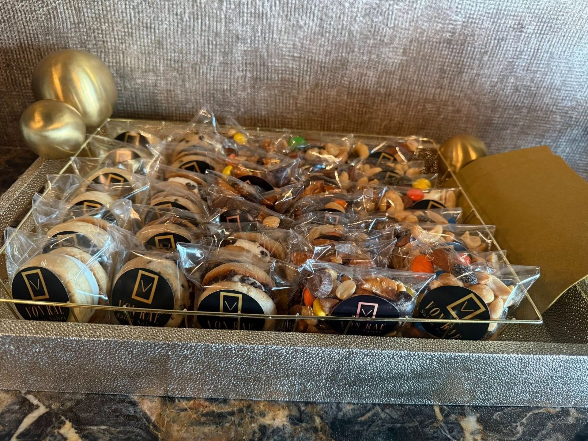 Gold and black wrapped gift favors arranged in a clear tray on a sparkly tablecloth, with gold ornaments nearby