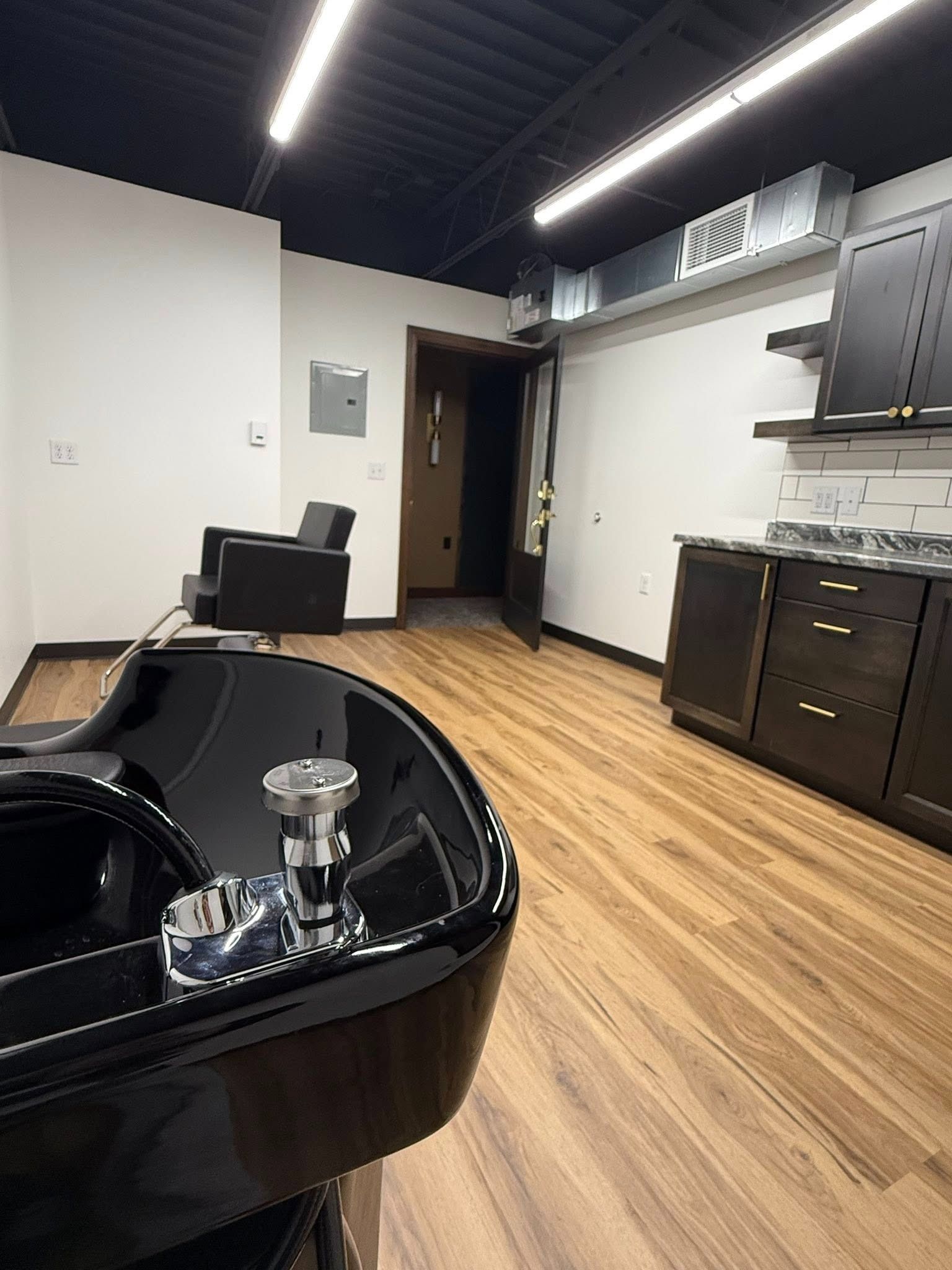 Modern salon interior with black styling chairs, wood floors, and white cabinets along the wall