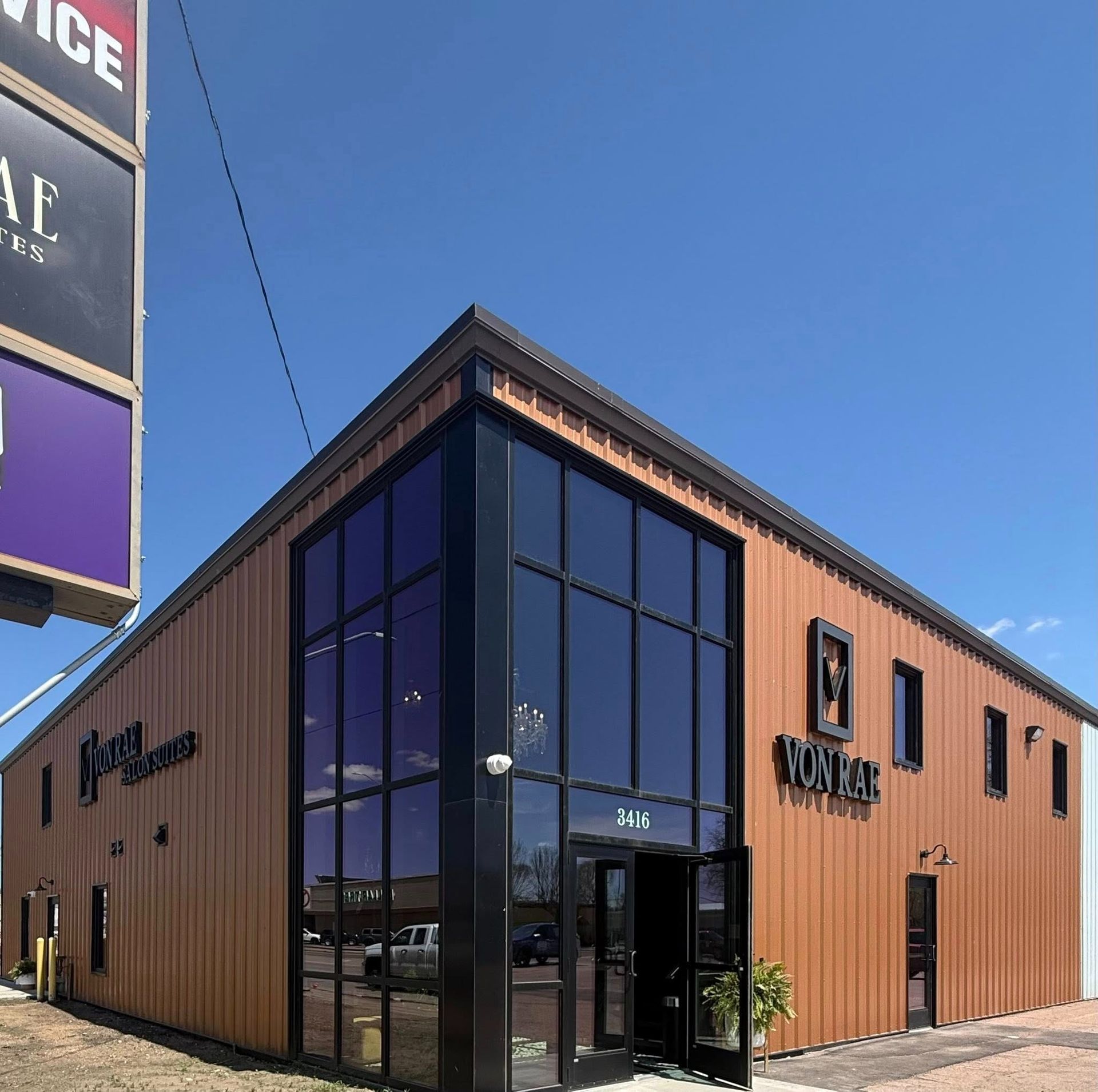 Modern wooden storefront with tall glass corner windows under a clear blue sky