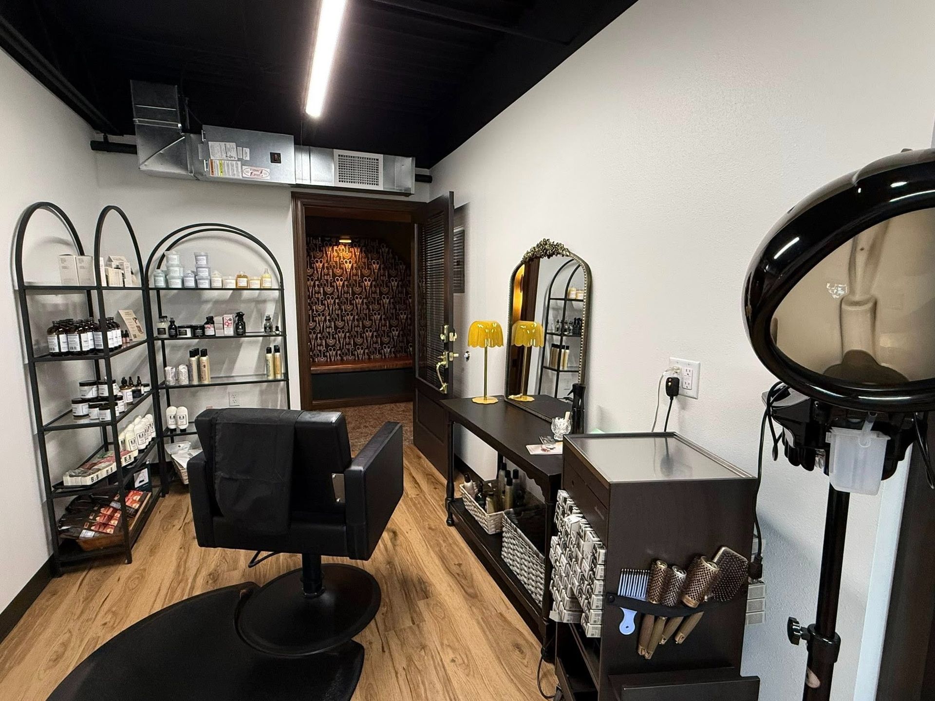 Modern salon interior with black styling chair, mirrors, shelves, and hair dryer station