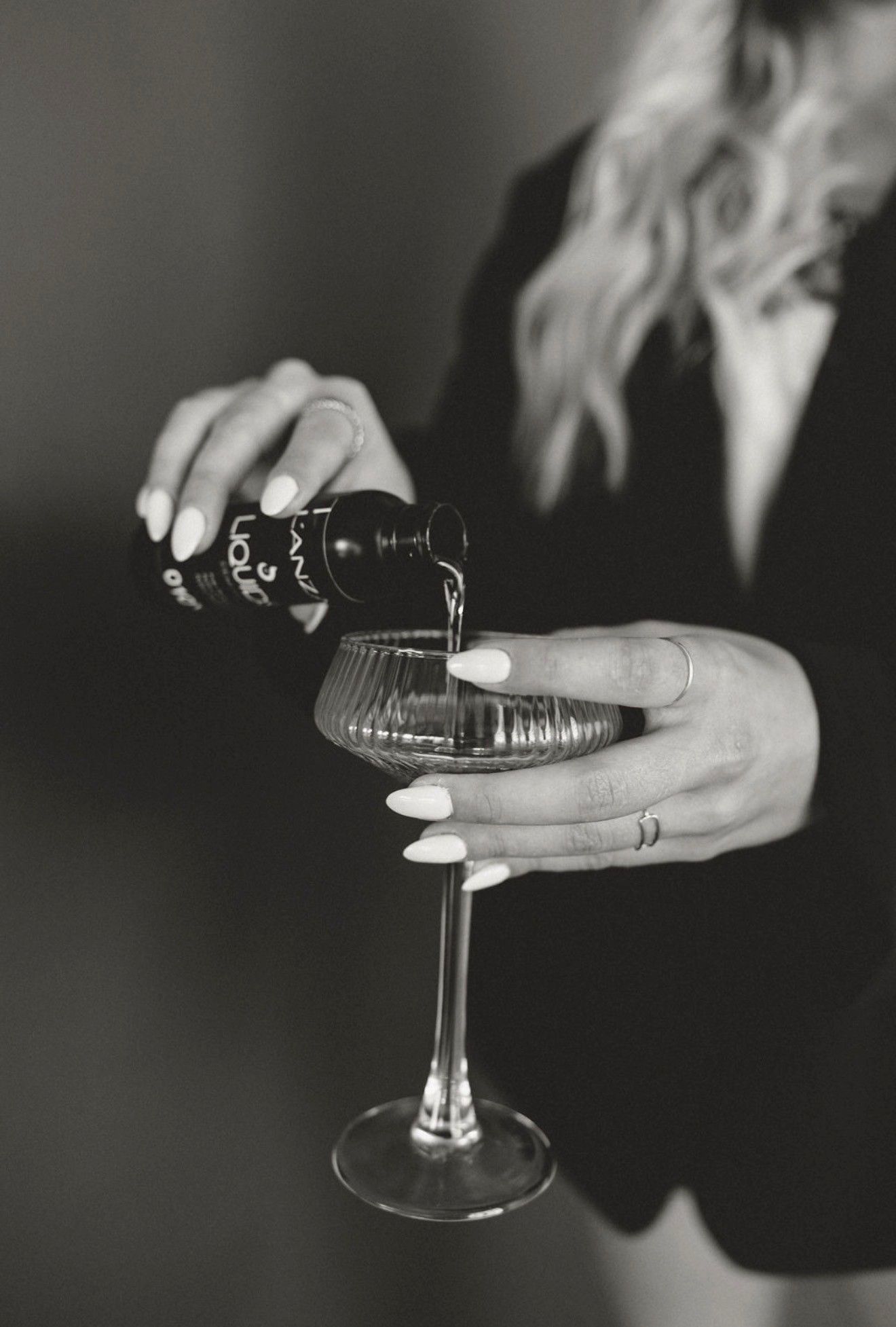 Black-and-white close-up of hands pouring champagne into a coupe glass from a bottle